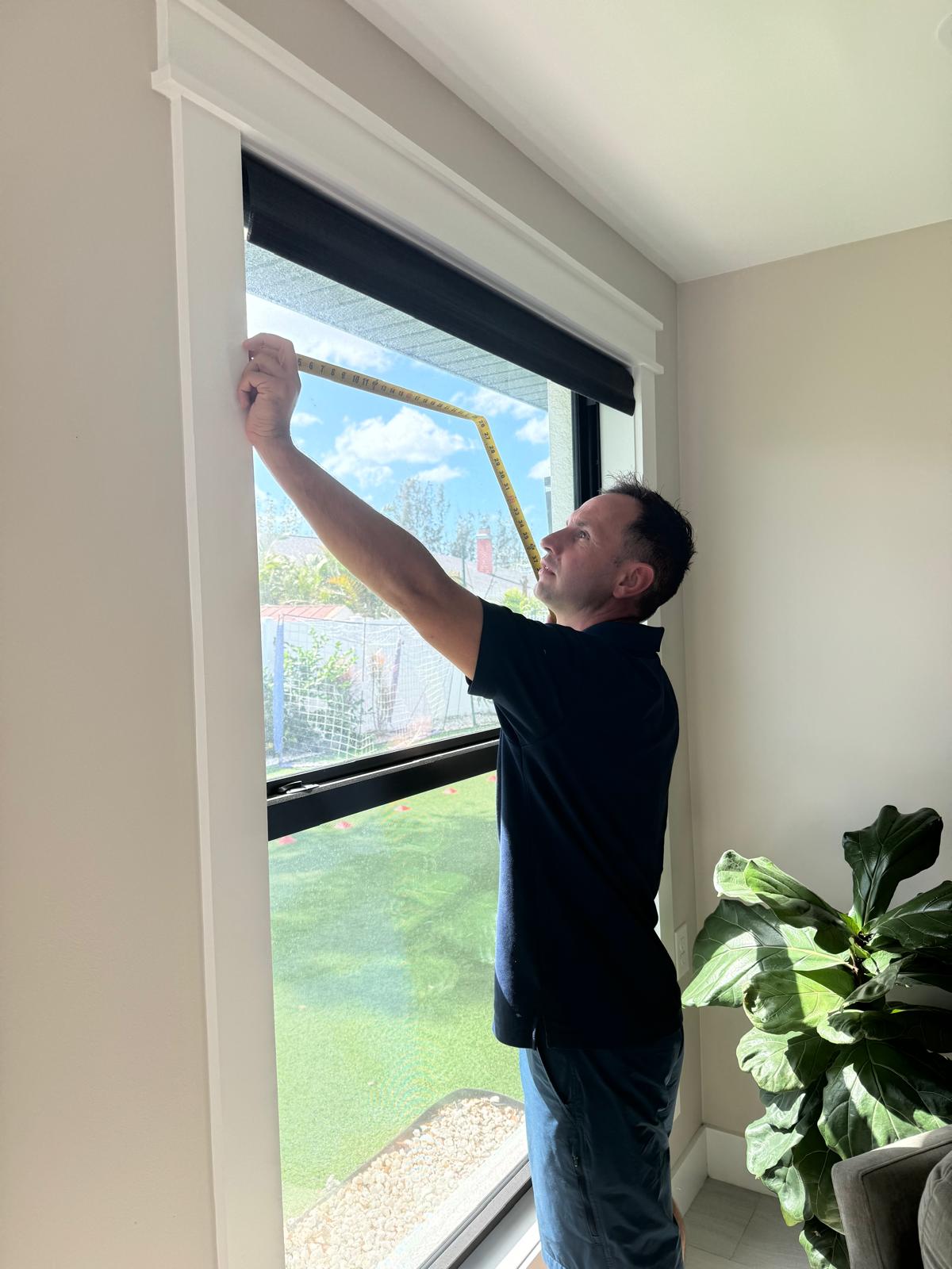 Gene Kann, owner of Finest Blinds, taking measurements of a customer's window to do a blind installation