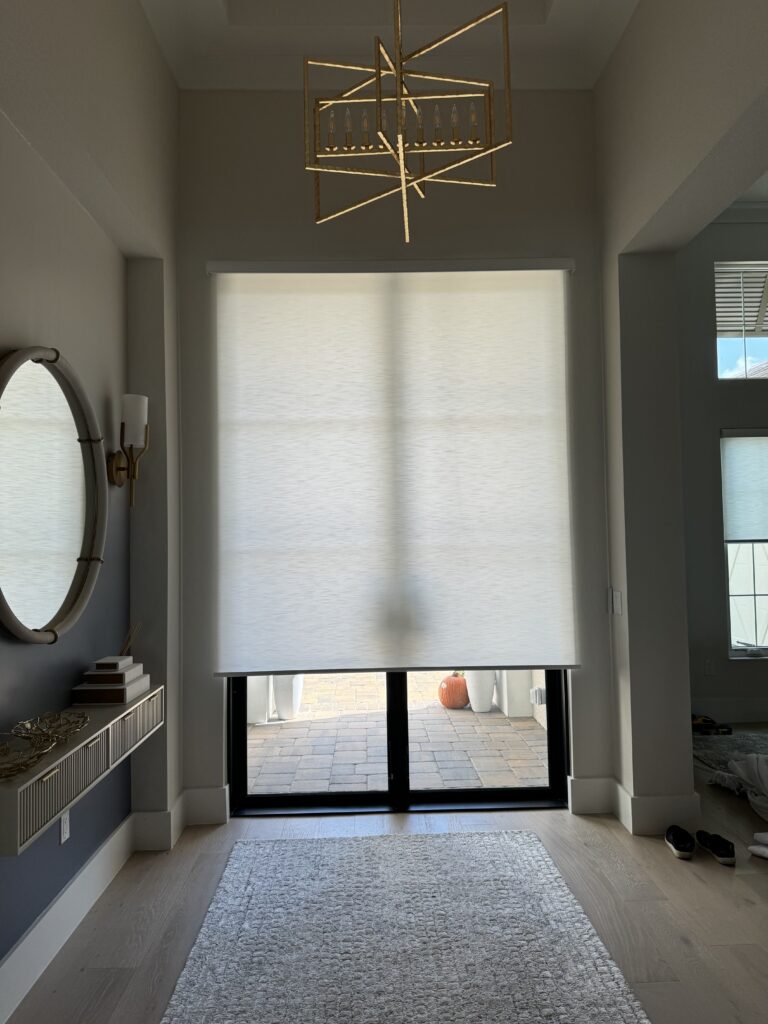 Elegant entryway in Lakewood Ranch featuring motorized roller shades as part of a whole-house installation, complemented by a modern gold chandelier and sleek decor